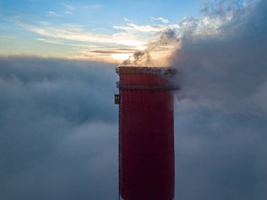 Gün batımında sislerin üzerinde bir termik santralin yüksek bacası. Hava aracı görünümü.