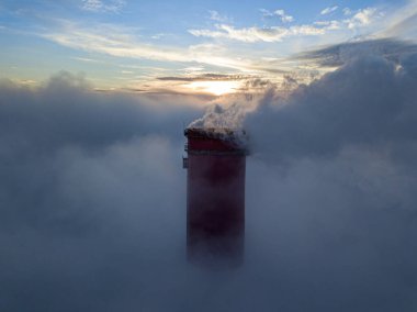 Gün batımında sislerin üzerinde bir termik santralin yüksek bacası. Hava aracı görünümü.