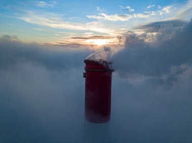 Gün batımında sislerin üzerinde bir termik santralin yüksek bacası. Hava aracı görünümü.