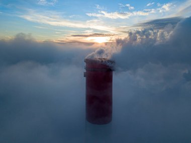 Gün batımında sislerin üzerinde bir termik santralin yüksek bacası. Hava aracı görünümü.