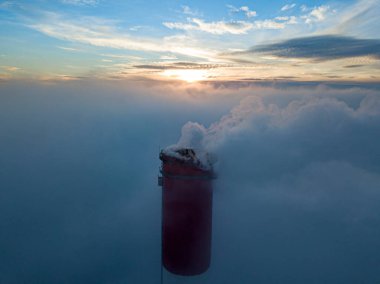 Gün batımında sislerin üzerinde bir termik santralin yüksek bacası. Hava aracı görünümü.