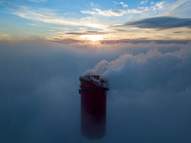 Gün batımında sislerin üzerinde bir termik santralin yüksek bacası. Hava aracı görünümü.