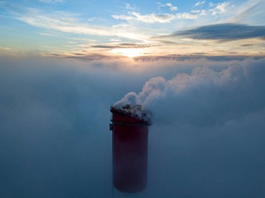 Gün batımında sislerin üzerinde bir termik santralin yüksek bacası. Hava aracı görünümü.
