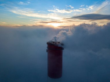 Gün batımında sislerin üzerinde bir termik santralin yüksek bacası. Hava aracı görünümü.