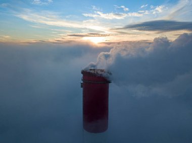 Gün batımında sislerin üzerinde bir termik santralin yüksek bacası. Hava aracı görünümü.