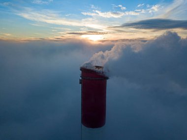 Gün batımında sislerin üzerinde bir termik santralin yüksek bacası. Hava aracı görünümü.