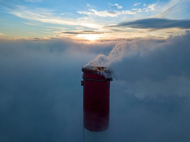 Gün batımında sislerin üzerinde bir termik santralin yüksek bacası. Hava aracı görünümü.