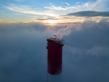 Gün batımında sislerin üzerinde bir termik santralin yüksek bacası. Hava aracı görünümü.