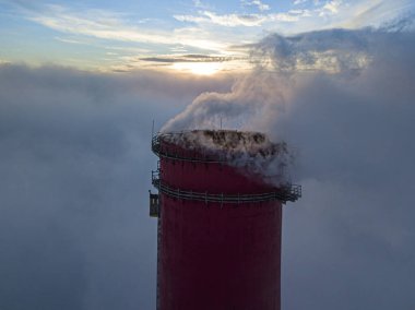 Gün batımında sislerin üzerinde bir termik santralin yüksek bacası. Hava aracı görünümü.