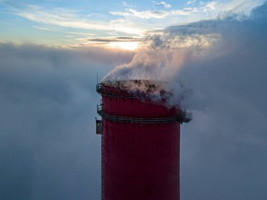 Gün batımında sislerin üzerinde bir termik santralin yüksek bacası. Hava aracı görünümü.
