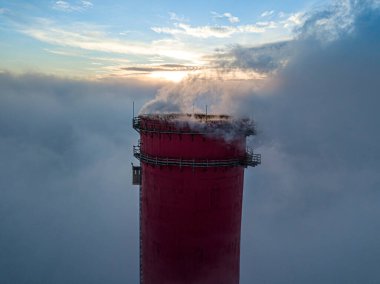 Gün batımında sislerin üzerinde bir termik santralin yüksek bacası. Hava aracı görünümü.