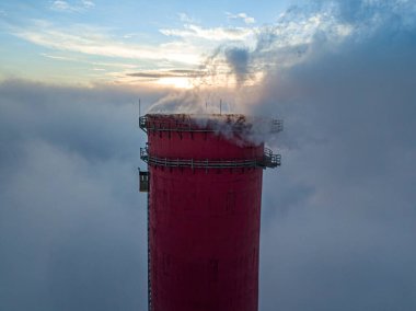 Gün batımında sislerin üzerinde bir termik santralin yüksek bacası. Hava aracı görünümü.