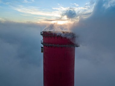 Gün batımında sislerin üzerinde bir termik santralin yüksek bacası. Hava aracı görünümü.