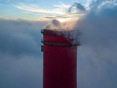 Gün batımında sislerin üzerinde bir termik santralin yüksek bacası. Hava aracı görünümü.