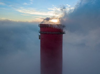Gün batımında sislerin üzerinde bir termik santralin yüksek bacası. Hava aracı görünümü.