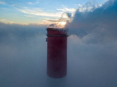 Gün batımında sislerin üzerinde bir termik santralin yüksek bacası. Hava aracı görünümü.