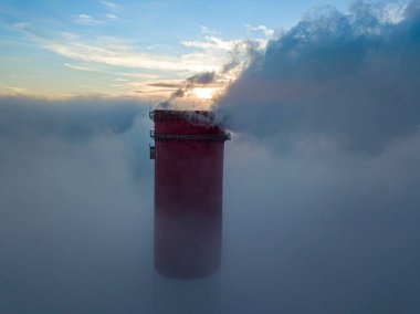 Gün batımında sislerin üzerinde bir termik santralin yüksek bacası. Hava aracı görünümü.