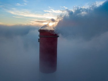 Gün batımında sislerin üzerinde bir termik santralin yüksek bacası. Hava aracı görünümü.