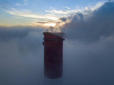 Gün batımında sislerin üzerinde bir termik santralin yüksek bacası. Hava aracı görünümü.