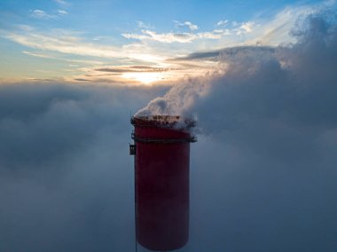 Gün batımında sislerin üzerinde bir termik santralin yüksek bacası. Hava aracı görünümü.