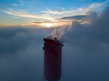 Gün batımında sislerin üzerinde bir termik santralin yüksek bacası. Hava aracı görünümü.