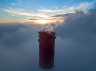 Gün batımında sislerin üzerinde bir termik santralin yüksek bacası. Hava aracı görünümü.