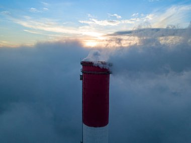 Gün batımında sislerin üzerinde bir termik santralin yüksek bacası. Hava aracı görünümü.