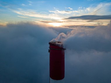 Gün batımında sislerin üzerinde bir termik santralin yüksek bacası. Hava aracı görünümü.
