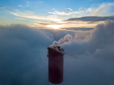 Gün batımında sislerin üzerinde bir termik santralin yüksek bacası. Hava aracı görünümü.
