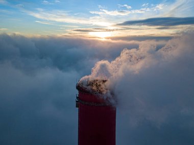 Gün batımında sislerin üzerinde bir termik santralin yüksek bacası. Hava aracı görünümü.