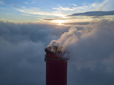 Gün batımında sislerin üzerinde bir termik santralin yüksek bacası. Hava aracı görünümü.
