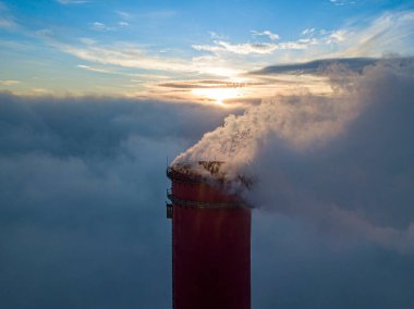 Gün batımında sislerin üzerinde bir termik santralin yüksek bacası. Hava aracı görünümü.