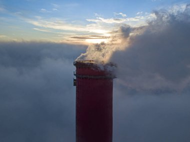 Gün batımında sislerin üzerinde bir termik santralin yüksek bacası. Hava aracı görünümü.