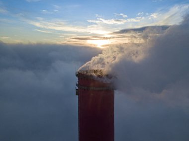 Gün batımında sislerin üzerinde bir termik santralin yüksek bacası. Hava aracı görünümü.