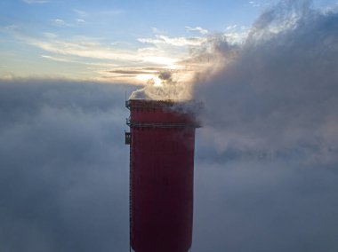 Gün batımında sislerin üzerinde bir termik santralin yüksek bacası. Hava aracı görünümü.