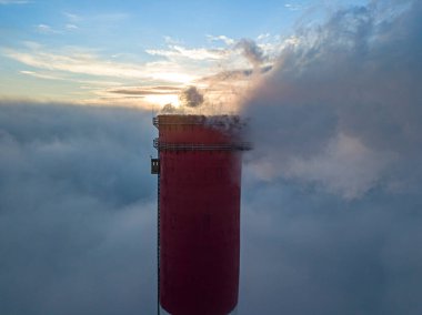 Gün batımında sislerin üzerinde bir termik santralin yüksek bacası. Hava aracı görünümü.