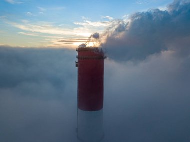 Gün batımında sislerin üzerinde bir termik santralin yüksek bacası. Hava aracı görünümü.