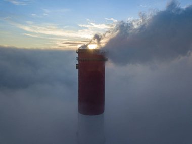 Gün batımında sislerin üzerinde bir termik santralin yüksek bacası. Hava aracı görünümü.