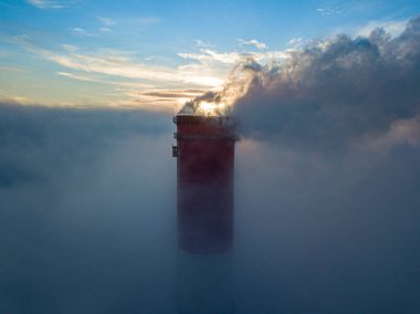 Gün batımında sislerin üzerinde bir termik santralin yüksek bacası. Hava aracı görünümü.