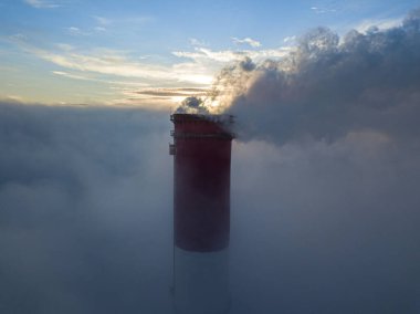 Gün batımında sislerin üzerinde bir termik santralin yüksek bacası. Hava aracı görünümü.