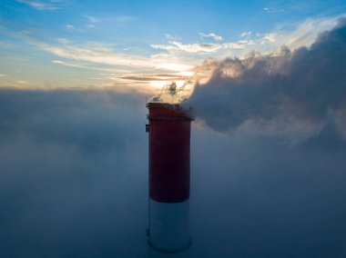 Gün batımında sislerin üzerinde bir termik santralin yüksek bacası. Hava aracı görünümü.