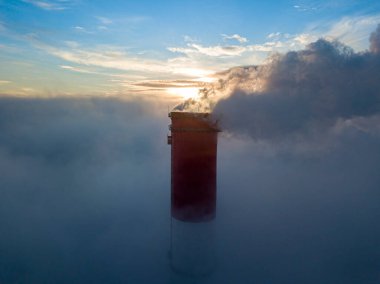 Gün batımında sislerin üzerinde bir termik santralin yüksek bacası. Hava aracı görünümü.