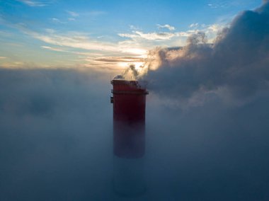 Gün batımında sislerin üzerinde bir termik santralin yüksek bacası. Hava aracı görünümü.