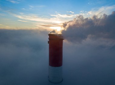 Gün batımında sislerin üzerinde bir termik santralin yüksek bacası. Hava aracı görünümü.