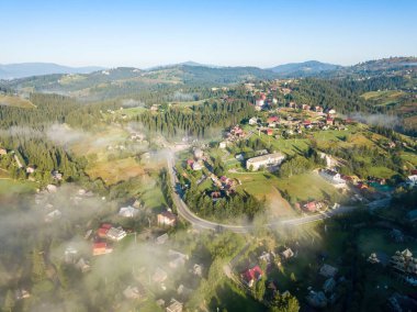 Bir dağ köyünün üzerinde ince bir sabah sisi. Sis dağların Ukrayna yamaçlarını kaplıyor. Hava aracı görünümü.