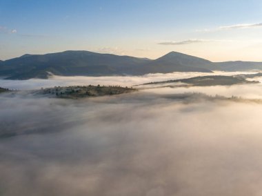 Ukrayna Karpatları 'nda yaz aylarında sislerin üzerinden uçarlar. Ufuktaki dağlar. Yoğun bir sis tabakası daimi bir halıyla dağları kaplar. Hava aracı görünümü.