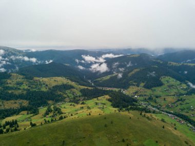 Yazın Ukrayna Karpat Dağları 'nın yeşil yamaçlarında. Bulutlu bir sabah, alçak bulutlar. Hava aracı görünümü.
