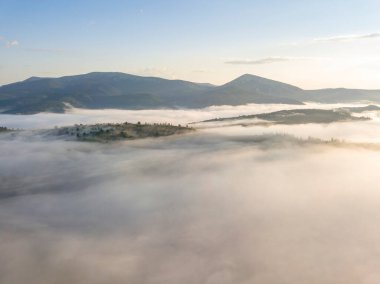 Ukrayna Karpatları 'nda yaz aylarında sislerin üzerinden uçarlar. Ufuktaki dağlar. Yoğun bir sis tabakası daimi bir halıyla dağları kaplar. Hava aracı görünümü.