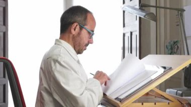 Resim stüdyosundaki çalışma masasında çizim yapan sanatçı..