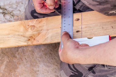 Elleri kalem ve inşaat cetvelini tutuyor ve tahtaya bir çizgi çekiyor..